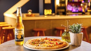 A table with a Corona Extra beer bottle, a pizza, and a potted plant. - Ibis budget London Heathrow Central (Hounslow)