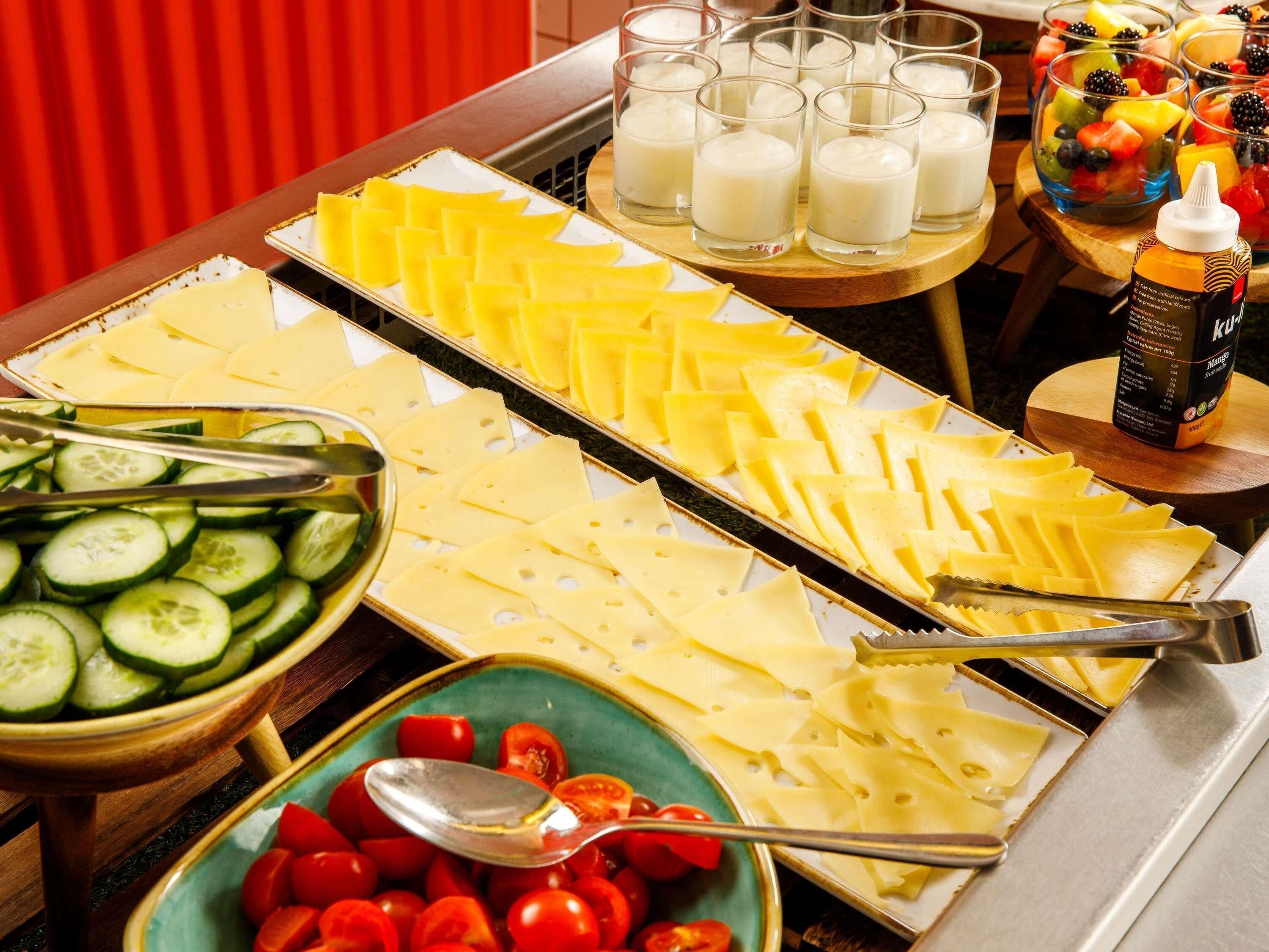 A buffet with cheese, cucumbers, tomatoes, milk, and fruit.