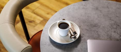 A round table with a cup of coffee and a spoon, a laptop, and a chair with a curved backrest.