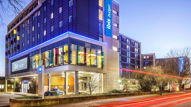A modern hotel with a prominent 'ibis budget' sign, a glass facade, and a parking area. - Ibis budget London Heathrow Central (Hounslow)