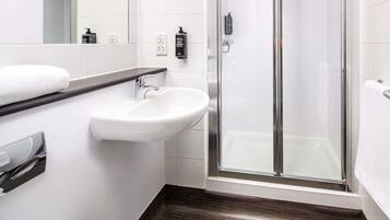 A modern bathroom with a white sink, a glass shower enclosure, and a dark wooden floor.