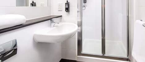 A modern bathroom with a white sink, a glass shower enclosure, and a dark wooden floor.