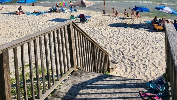 Una passerella di legno che conduce a una spiaggia sabbiosa con ombrelloni e lettini.