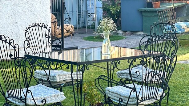 Een terras buiten, met een ronde tafel en zwarte metalen stoelen, omgeven door een bakstenen muur en een overdekt gedeelte.
