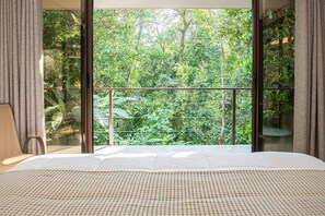 A bedroom with a large window offering a view of lush greenery outside.