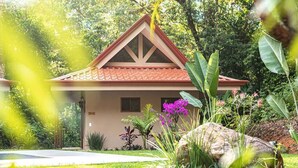 Una casa con techo de tejas rojas, rodeada de abundante follaje y plantas en flor.