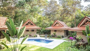 Un resort con tres edificios tipo bungaló, una piscina y abundante vegetación.