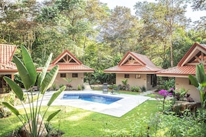 A resort with three bungalow-style buildings, a swimming pool, and lush greenery.