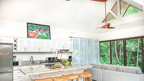 Cocina moderna con una isla central, taburetes de bar y un amplio ventanal con vistas a zonas verdes.
