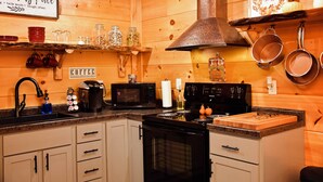 A kitchen with wooden walls, a stove, microwave, and various kitchen utensils.