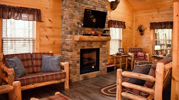 A cozy log cabin interior with a stone fireplace, plaid furniture, and a mounted deer head.