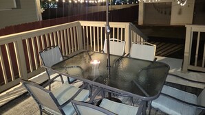 Ein Tisch mit Glasplatte und vier Stühlen unter einer Markise, umgeben von einer Holzterrasse mit Geländern.