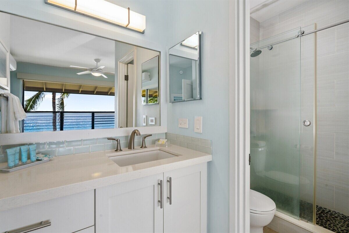 A bathroom with a large mirror, a sink, and a glass-enclosed shower.