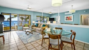 A spacious living room with a glass dining table, comfortable seating, and a view of the ocean. - Poipu Shores 402A - Full A/C Luxury, Sublime Views (Koloa)