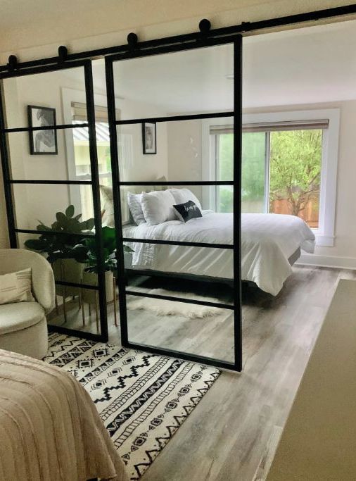 A bedroom with a large bed, a mirrored partition, a white chair, and a patterned rug.