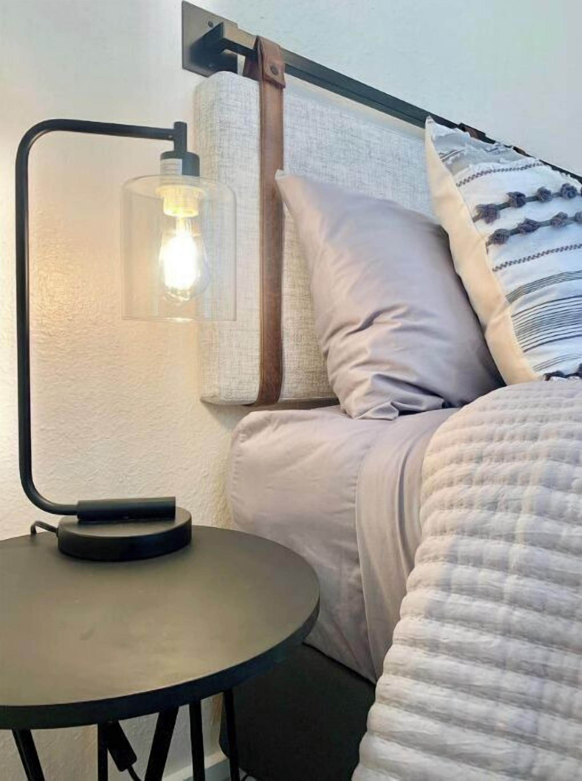 A bed with a headboard, a bedside table with a lamp, and a pillow.