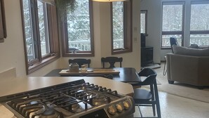 Une cuisine moderne équipée d’une cuisinière et d’un four à gaz, de grandes fenêtres donnant sur un paysage enneigé, et un coin repas avec une table et des chaises.
