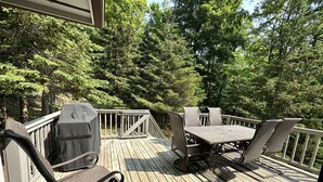 Une terrasse en bois aménagée avec du mobilier d’extérieur, notamment une table et des chaises, ainsi qu’un barbecue.