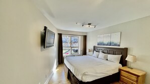 A bedroom with a large bed, a TV mounted on the wall, a ceiling fan, and a window with curtains. - Best ski in ski out Condo at Whistler (whistler)