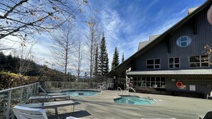 A pool area with lounge chairs and a building with a circular window. - Best ski in ski out Condo at Whistler (whistler)
