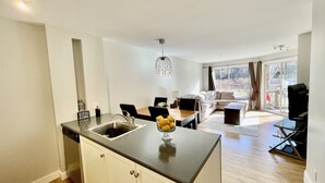 A modern kitchen with a central island, a dining area with a table and chairs, and a living room with a sofa and a large window. - Best ski in ski out Condo at Whistler (whistler)