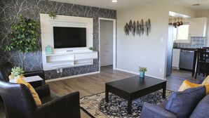 A modern living room with a flat-screen TV, dark sofas, a coffee table, and a patterned rug. - Over the Oaks - Great View - Whole Home - Stylish  (Thousand Oaks)