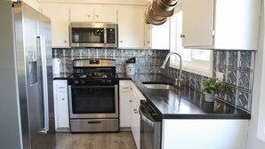 A modern kitchen with stainless steel appliances, white cabinetry, and a black countertop. - Over the Oaks - Great View - Whole Home - Stylish  (Thousand Oaks)
