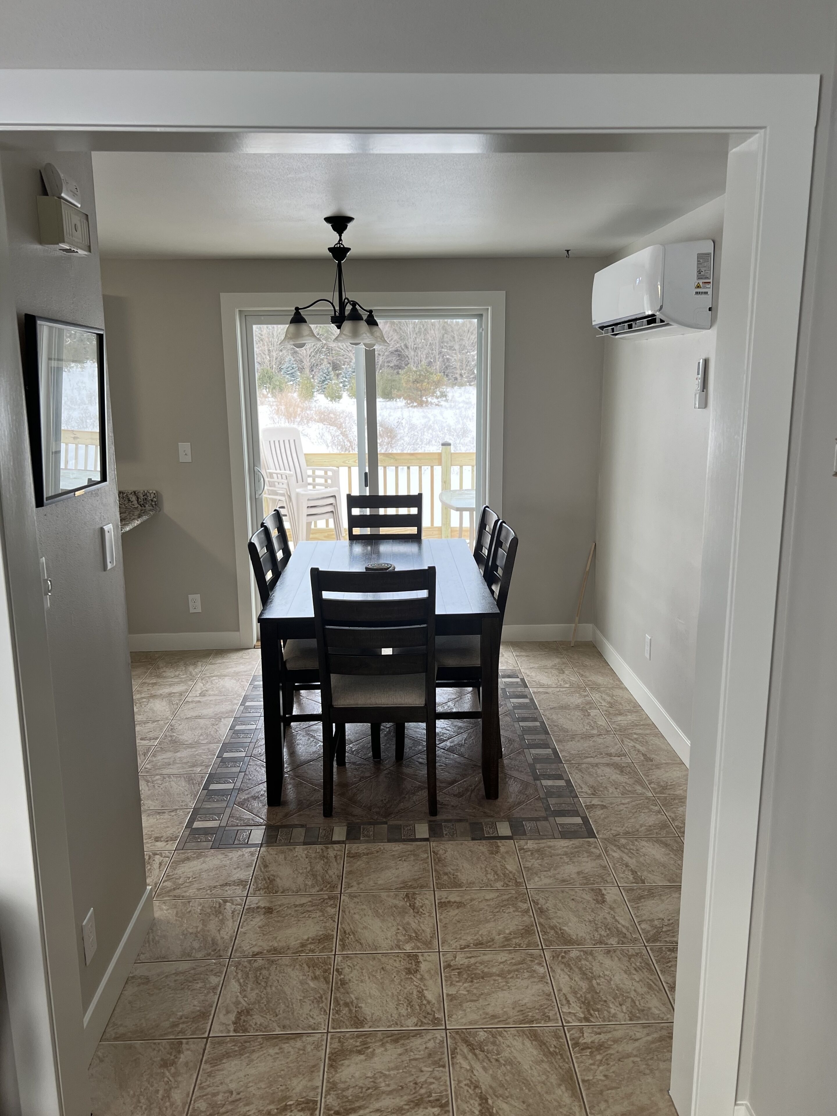 Un coin repas avec une table et des chaises, un ventilateur de plafond et une vue sur une terrasse enneigée, visible à travers une grande fenêtre.