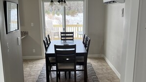 Een eethoek met een tafel en stoelen, een plafondventilator en uitzicht op een besneeuwde veranda door een groot raam.