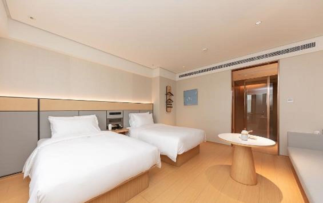 A hotel room with two beds, a small table, and a sofa.