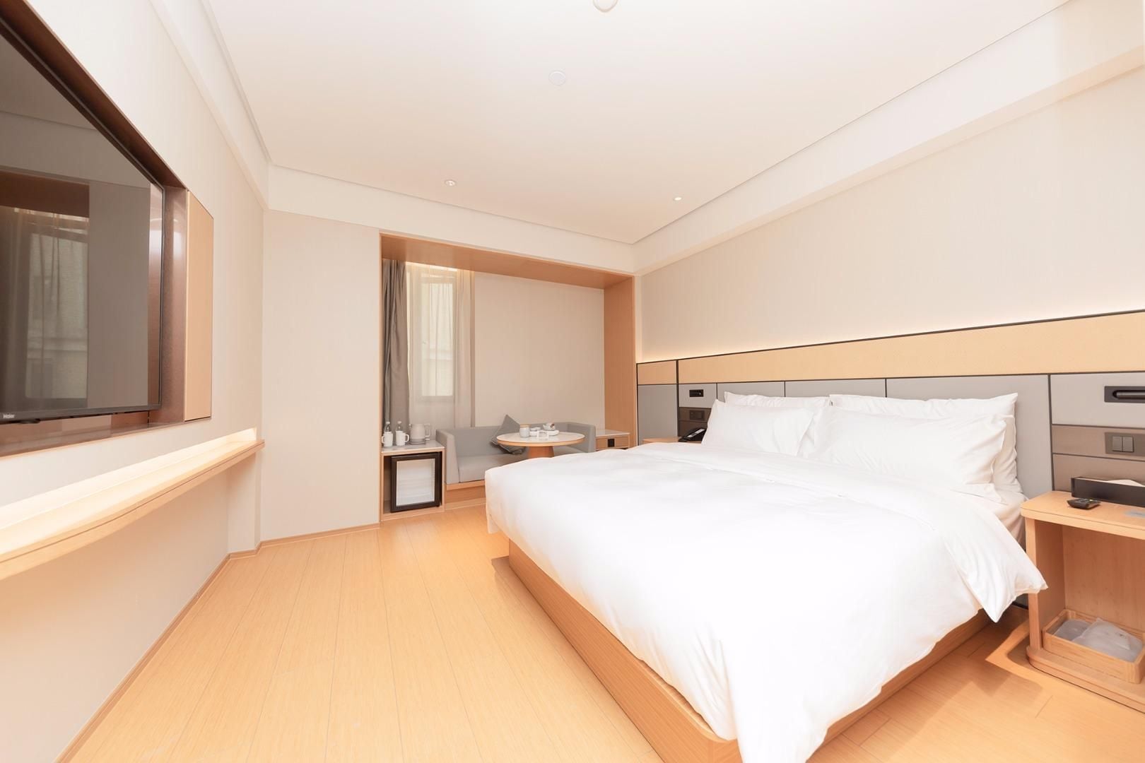 A modern hotel room with a large bed, bedside tables, a TV, and a small seating area.