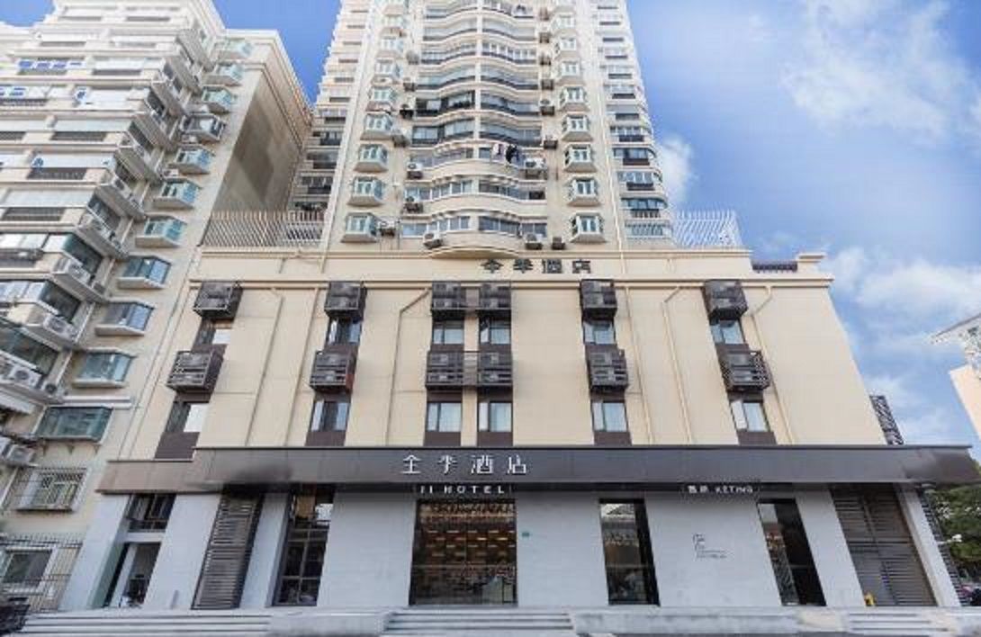 Um edifício de hotel com várias varandas, uma placa indicando ser um hotel, e um céu azul ao fundo.