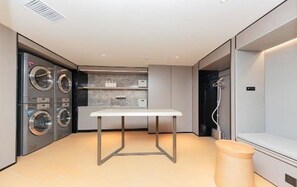 A modern laundry room with built-in washers and dryers, a table, and a trash bin.