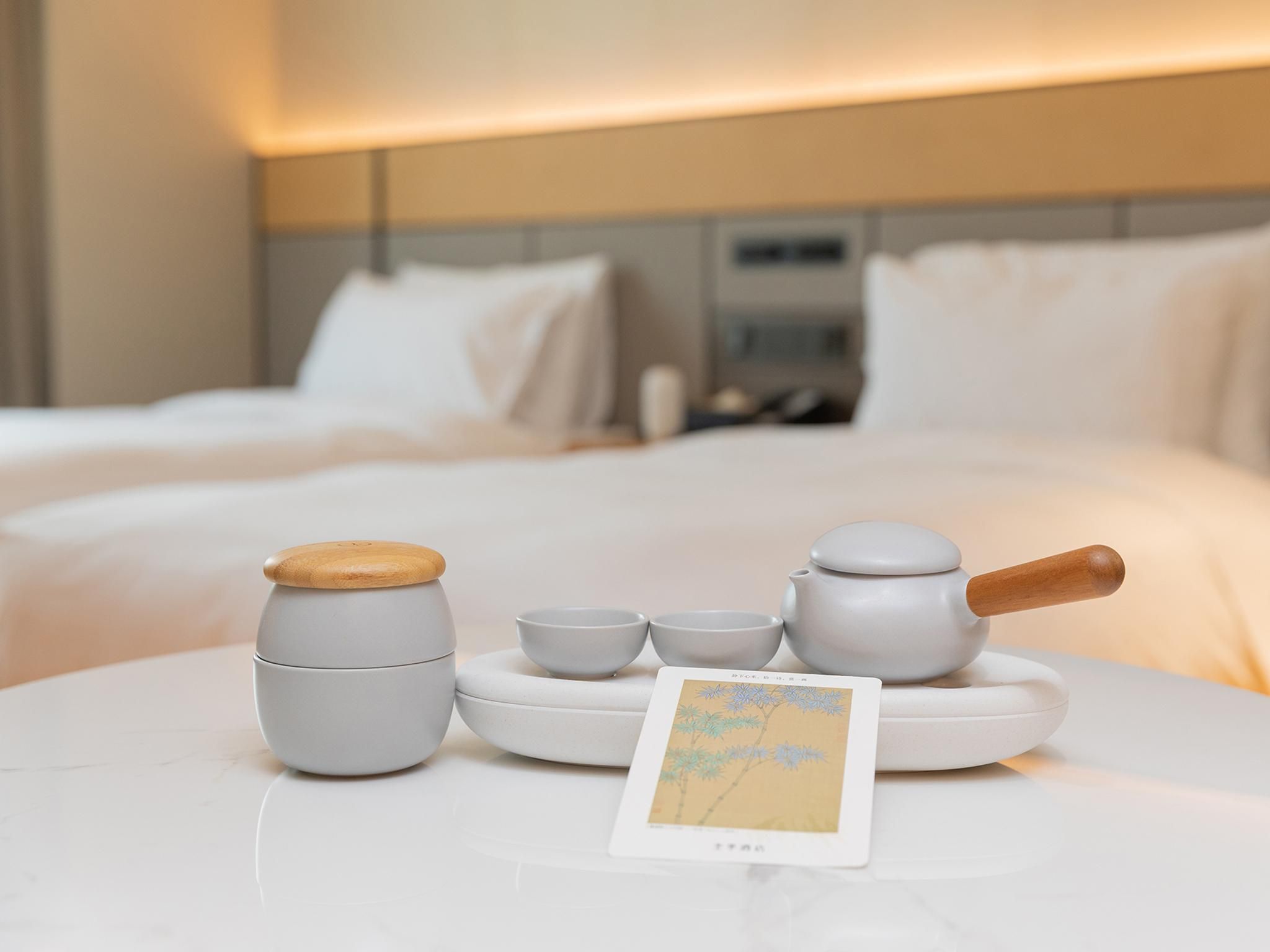 A neatly arranged tea set on a white table in a hotel room with a bed in the background.