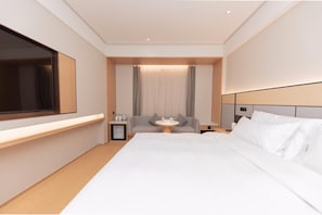 Una habitación de hotel moderna con una cama grande, un televisor de pantalla plana, una mesita de noche con lámpara y una zona de estar con mesa y sillas.