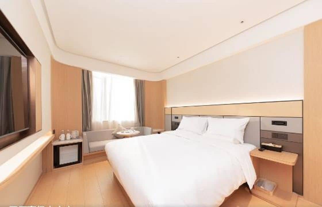 A hotel room with a large bed, bedside tables, a TV, and a window with curtains.
