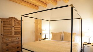 Una cama con dosel y tablero de madera, un aparador de madera con cajones y dos mesitas de noche con lámparas.