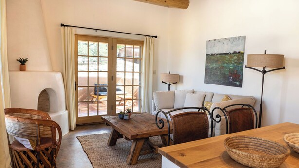 Una sala de estar acogedora con chimenea, un sofá, una mesa de comedor y vistas a un patio exterior a través de amplios ventanales.