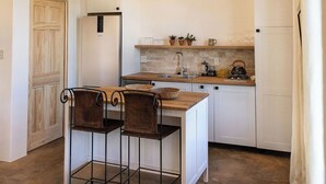 Una cocina compacta con vigas de madera en el techo, un refrigerador blanco, un lavamanos y una pequeña encimera. Hay dos sillas y una mesa en el centro.