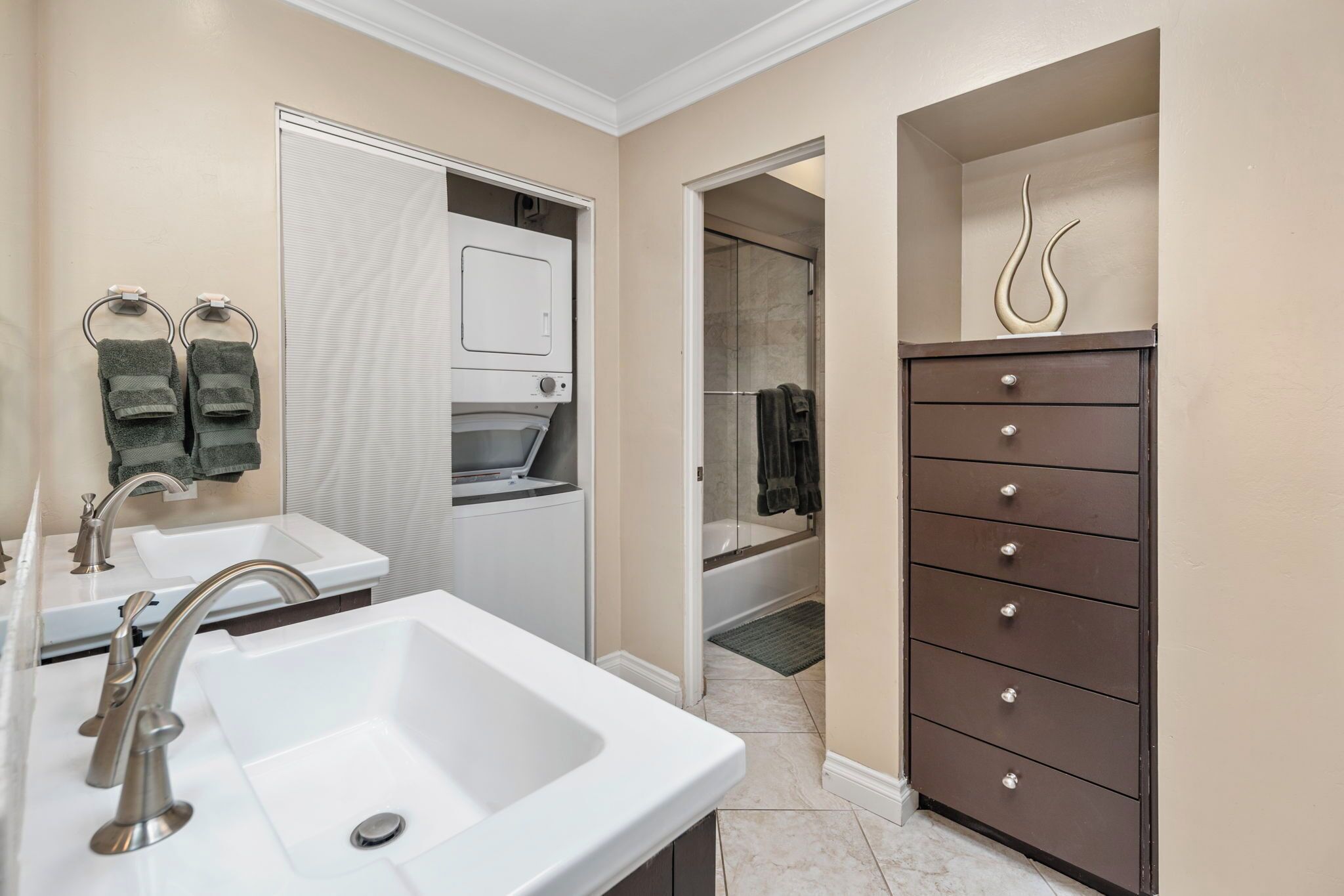 A modern bathroom with a white sink, two towel rings, a dark wooden cabinet, and a shower area.