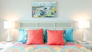 A bedroom with a colorful quilt, two red pillows, and a painting of a coastal town on the wall. - Stunning, renovated 3/2 condo on the beach, 2 large Ocean front pools. Sleeps 8 (Panama City Beach)