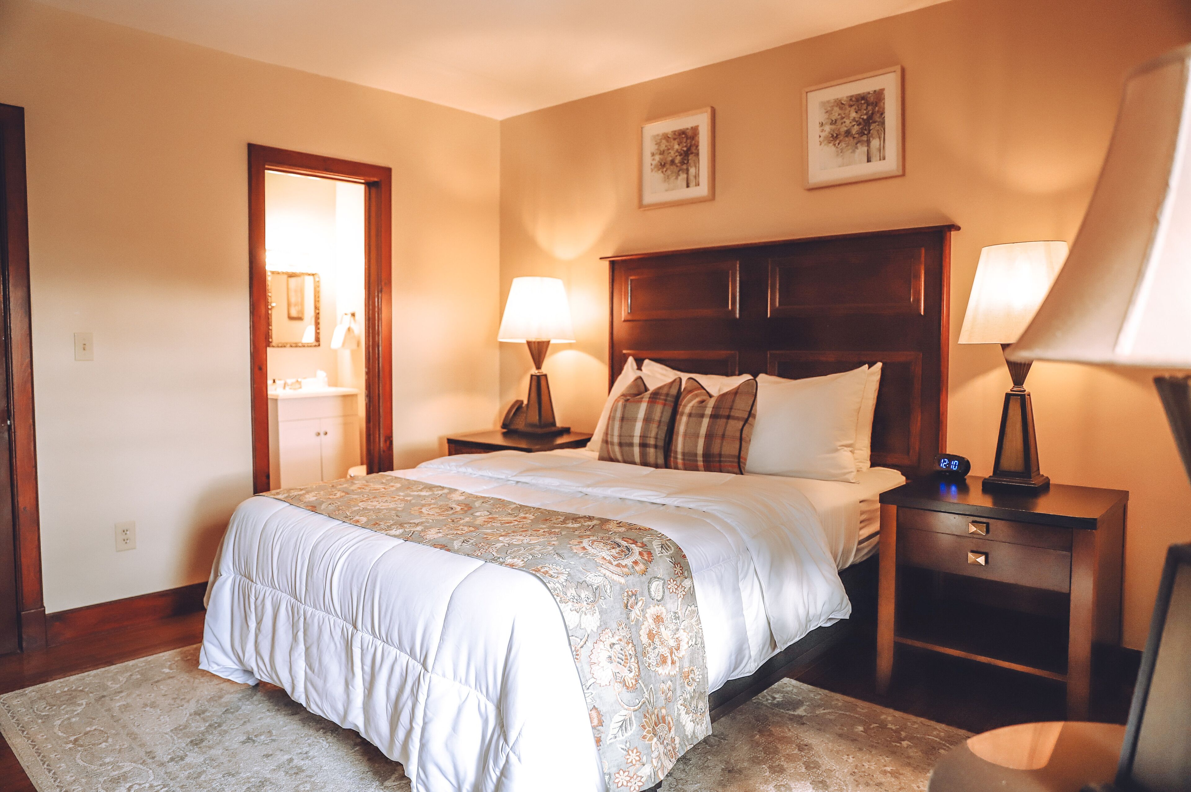 Une chambre à coucher avec un grand lit, deux tables de chevet avec des lampes, une tête de lit en bois et une porte donnant sur une salle de bain.