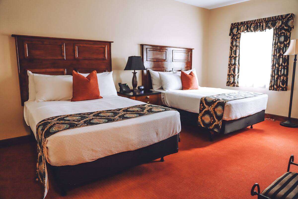 A hotel room with two beds, a nightstand with a lamp, and a window with curtains.