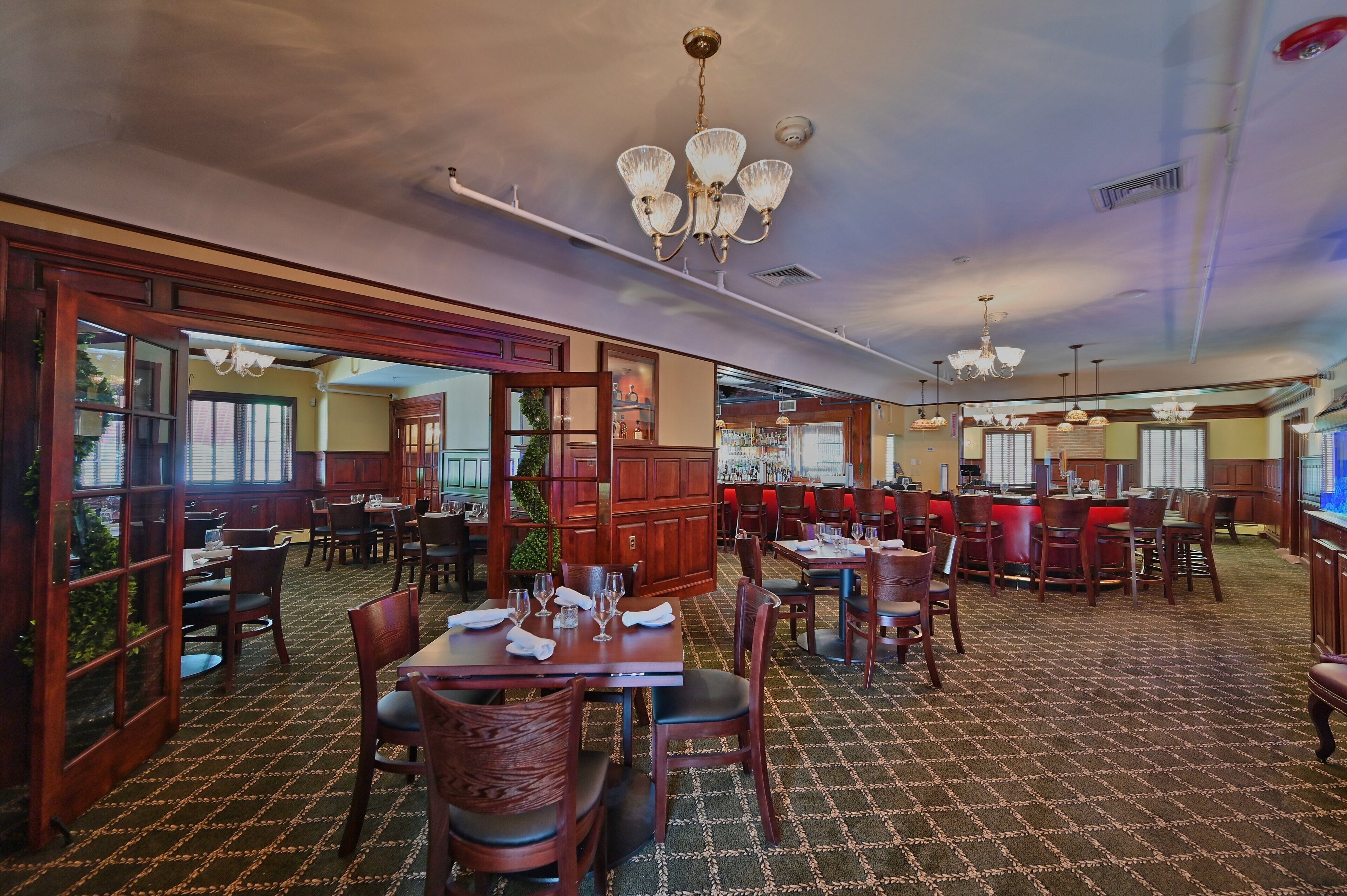 Restaurante com mobiliário de madeira, lustres e tapete estampado.