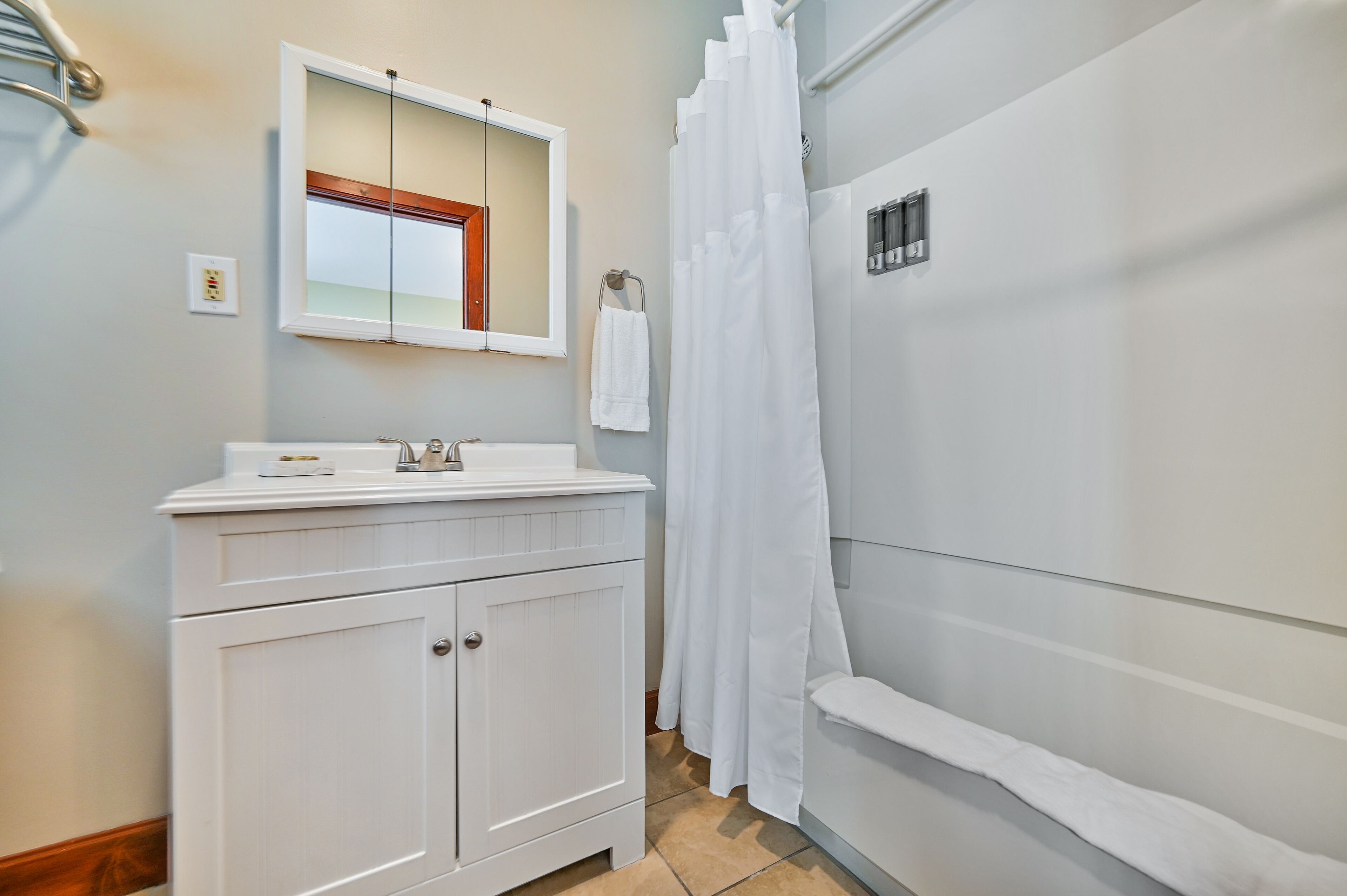 A bathroom with a white vanity, a mirror, a towel rack, and a shower curtain.