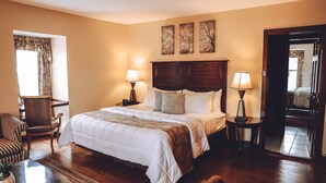 Un dormitorio ordenado con una cama grande, dos mesitas de noche con lámparas, una silla y una ventana con cortinas.
