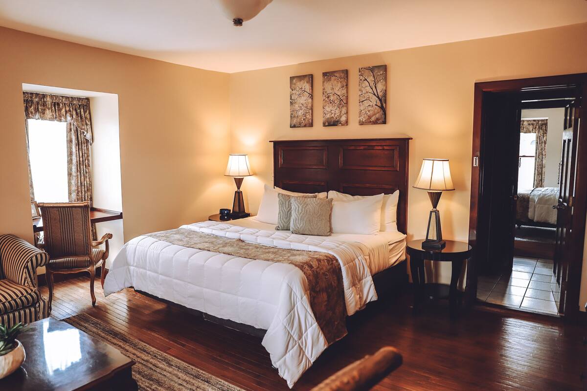 A neatly arranged bedroom with a large bed, two bedside tables with lamps, a chair, and a window with curtains.