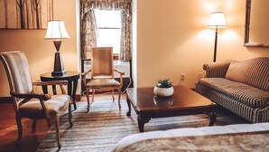 Una habitación de hotel acogedora con suelo de madera, un sofá a rayas, una mesa de centro de madera, una silla, una lámpara y un cuadro en la pared.