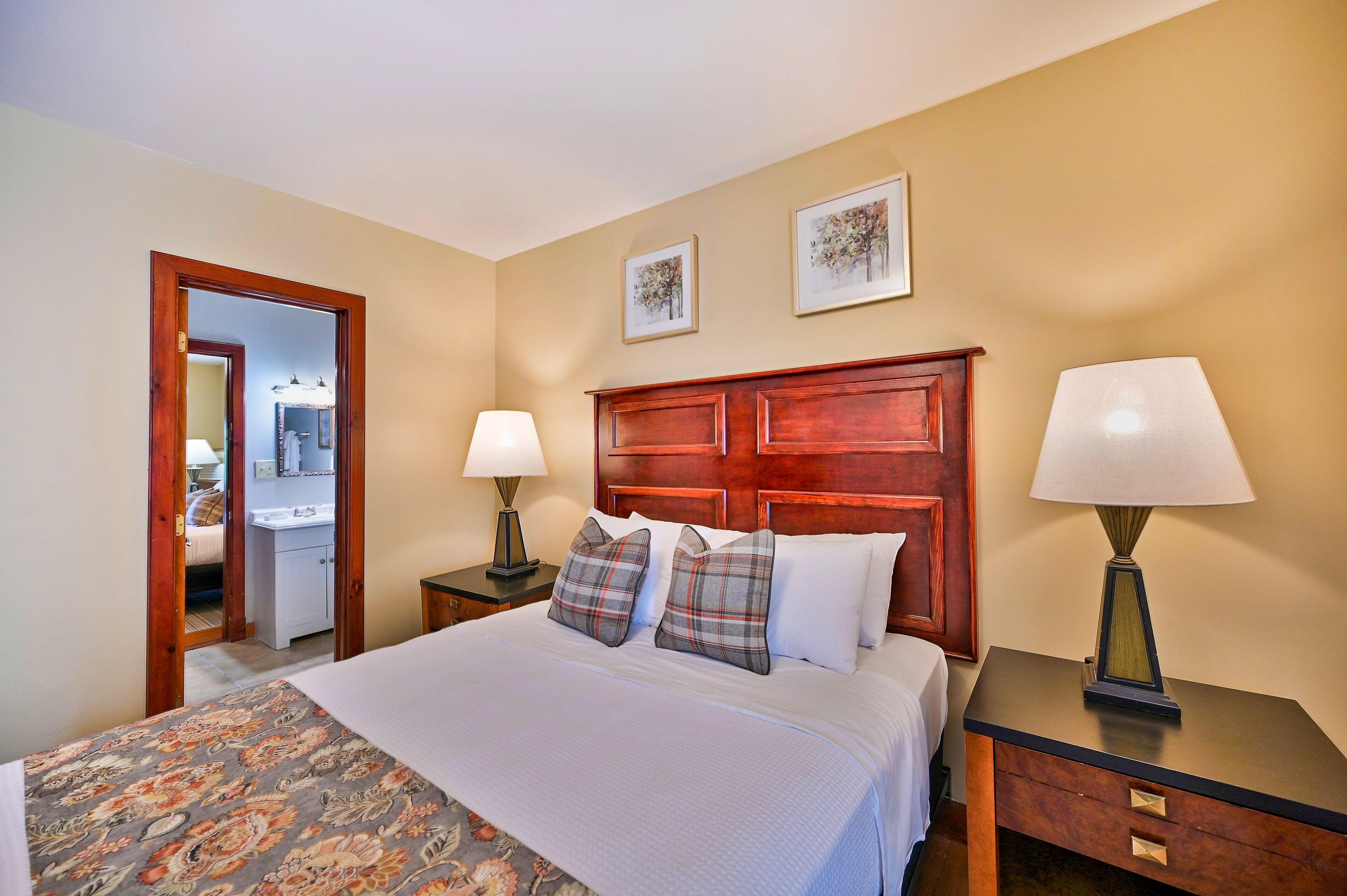 Une chambre d’hôtel avec un grand lit, deux tables de chevet avec des lampes, une tête de lit en bois et une porte donnant sur une salle de bain.