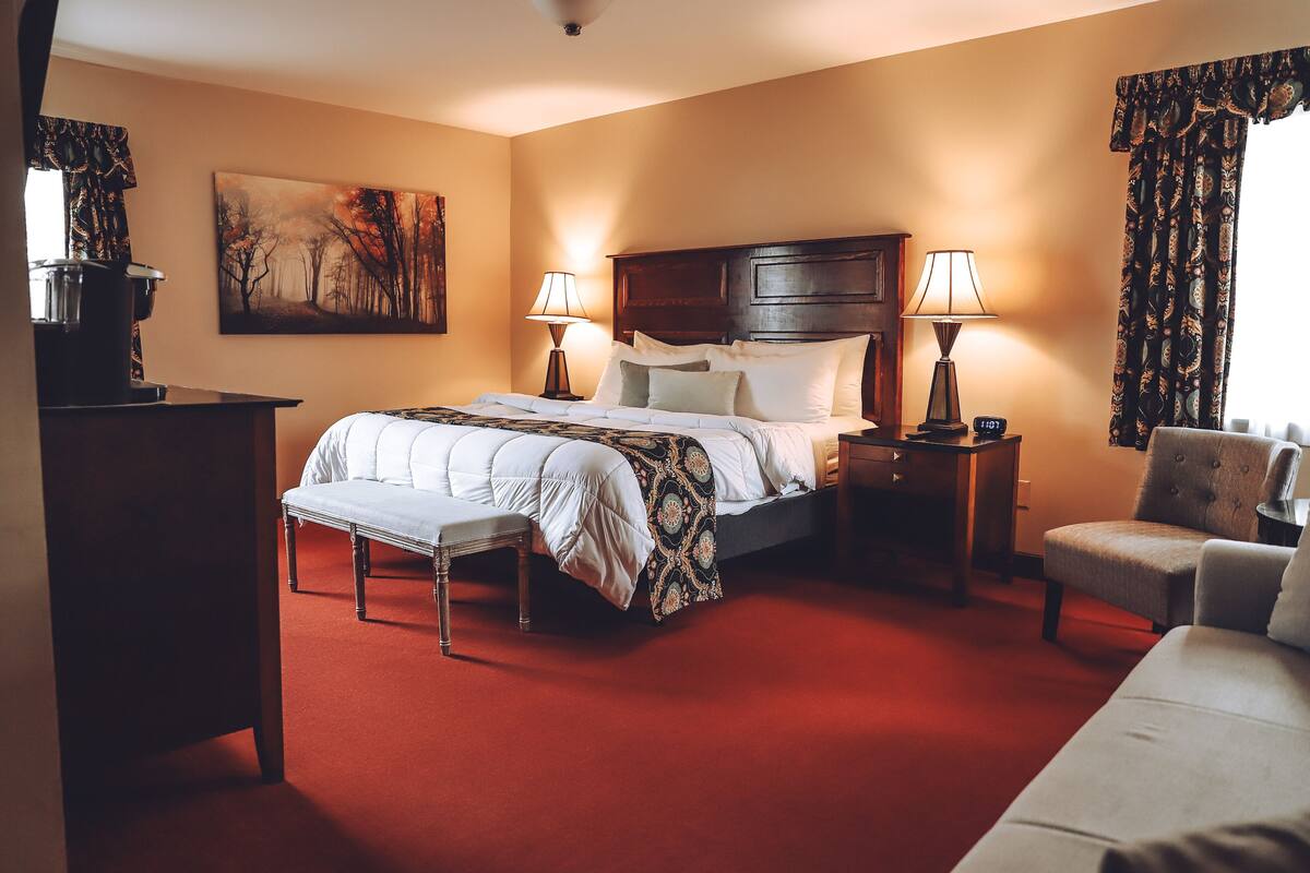 A hotel room with a large bed, two bedside tables with lamps, a chair, a desk with a lamp, and a painting on the wall.